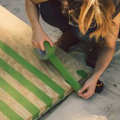 a woman sanding down some boards with green tape