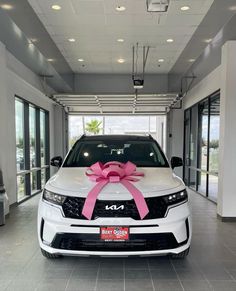 a white car with a pink bow on it's hood in a showroom