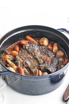 a pot filled with meat and vegetables on top of a white table next to utensils