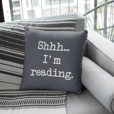 a pillow that says shh i'm reading sitting on top of a couch