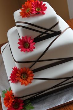 a three tiered cake with flowers on it sitting on top of a wooden table