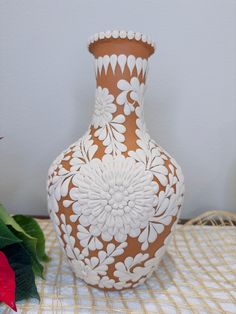 a brown and white vase sitting on top of a table next to a red flower