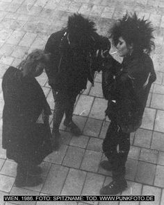 two men with black hair standing next to each other in front of a brick floor