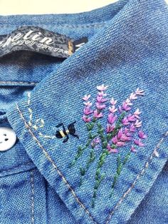 a blue jean jacket with pink flowers embroidered on the front and back pocket, along with a white button