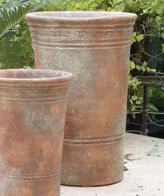 two large clay pots sitting on top of a cement slab next to plants and bushes