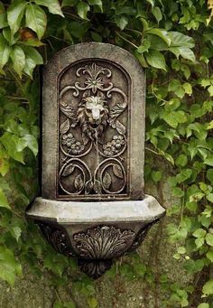 a stone fountain in the shape of a lion's head surrounded by green leaves