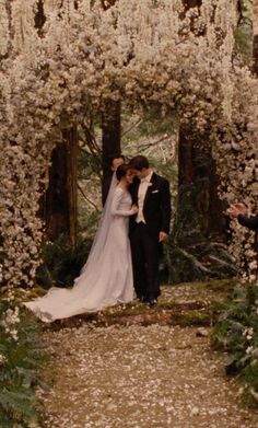 a bride and groom standing under an archway with white flowers on the trees in front of them