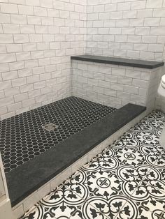 a white toilet sitting next to a black and white tiled floor in a room with tile walls