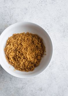 a white bowl filled with brown sugar on top of a marble counter next to a spoon