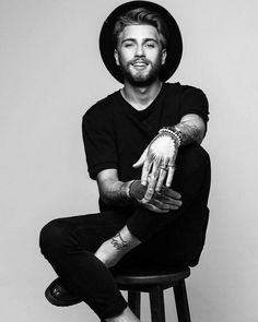 a man sitting on top of a stool wearing a hat and holding his hands up