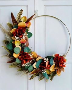 a wreath made out of fake flowers and leaves on a white door with the letter o