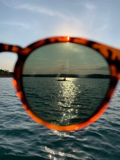 a pair of sunglasses reflecting the sun over water with a boat in the back ground