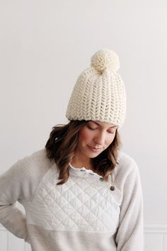 a woman wearing a white knitted hat with a pom - pom on top