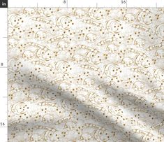 a white and gold fabric with small flowers on the side, in front of a ruler