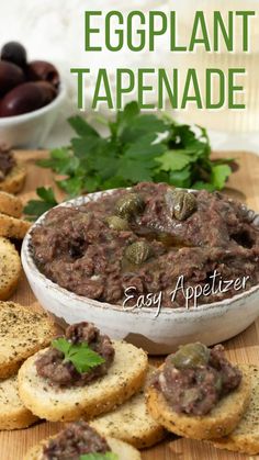 an eggplant tapenade in a white bowl surrounded by crackers and olives