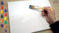 a person holding a paintbrush over a white sheet of paper with colored drops on it