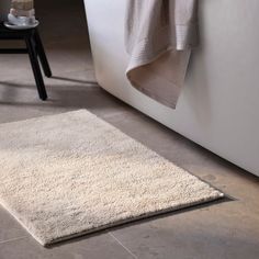 a bathroom with a white bathtub and rug on the floor, next to a black stool