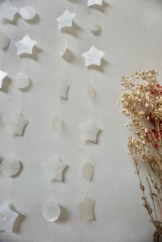 some white stars are hanging on the wall next to dried flowers and vase with red berries