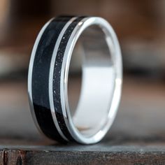 a wedding ring with black and white inlays on the inside, sitting on top of a piece of wood