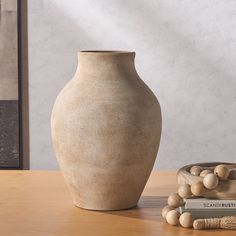 a white vase sitting on top of a wooden table next to a bowl and book