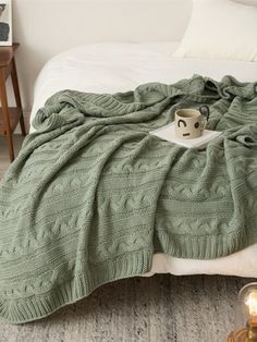 a green blanket on top of a bed next to a tea cup and candle in front of it