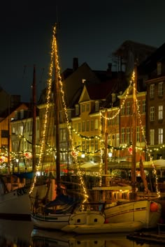 several boats are docked in the water near buildings with christmas lights on them at night