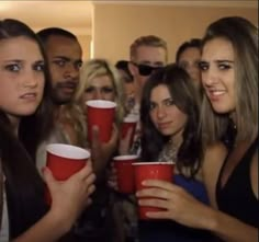 a group of people standing around each other holding red cups in front of their faces