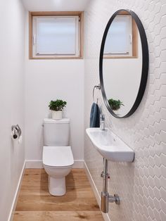 a white toilet sitting next to a bathroom sink under a round mirror on a wall