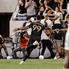 two men playing soccer on a field with fans in the stands watching from behind them