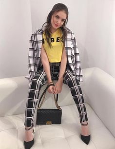 a woman sitting on a white couch holding a handbag and posing for the camera