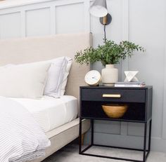 a bedroom with a bed, nightstand and plants on the side table in front of it