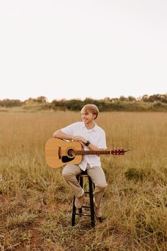 a man sitting on a stool playing an acoustic guitar in a field with tall grass