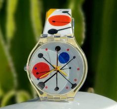 a colorful watch sitting on top of a white table next to a green leafy plant