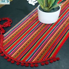 a potted plant sitting on top of a table next to a colorful rug with pom poms