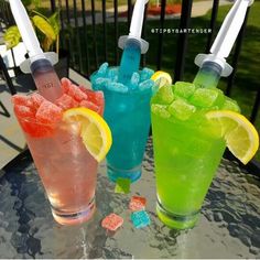 three different colored drinks sitting on top of a table next to each other with lemon wedges