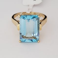 a ring with an aqua topazte surrounded by yellow gold trimmings on a white background