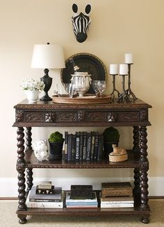 a wooden table topped with lots of books next to a wall mounted clock and lamp