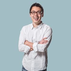 a man with glasses is smiling while standing in front of a blue background and wearing a white shirt