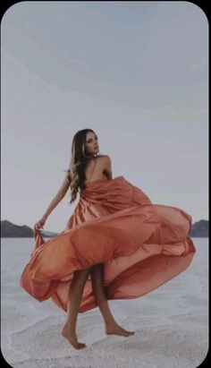 a woman in an orange dress is walking on the sand with her legs spread out