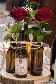 three wine bottles with roses in them tied to the top and sitting on a tree stump