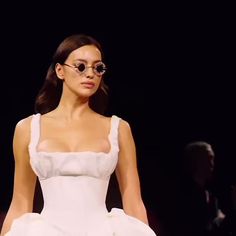 a woman in a white dress walking down a runway