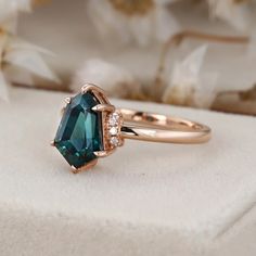 an engagement ring with a green stone surrounded by diamonds on a white surface next to flowers