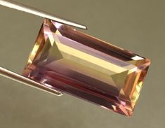 an orange and pink tourmaline stone is being held by a pair of tongs