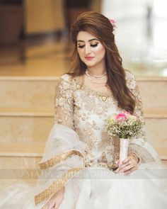 a woman in a wedding dress sitting on the stairs with flowers and holding a bouquet