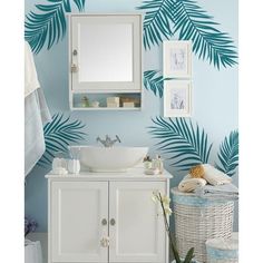 a white sink sitting under a bathroom mirror next to a wall with palm leaves on it