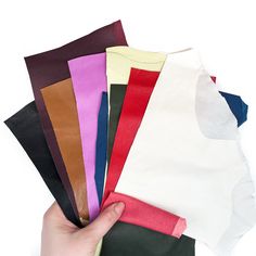 a hand is holding several different colored pieces of paper in front of each other on a white surface