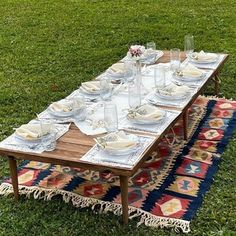 a table set up with plates and silverware on top of a rug in the grass