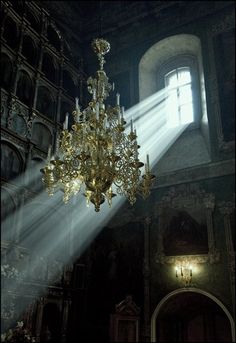 a chandelier in the middle of a dark room with light streaming through it