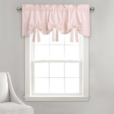 a white chair sitting in front of a window with pink bow valances on it