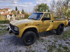 a yellow pick up truck parked on top of a gravel road